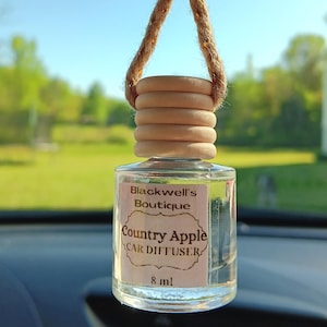 May include: A clear glass bottle with a brown wooden cap and a beige string hanging from it. The bottle contains a car diffuser with a label that reads "Blackwell's Boutique Country Apple Car Diffuser 8 ml".