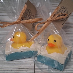 May include: Two yellow rubber ducky soaps in clear cellophane bags, tied with raffia. Each soap features a yellow duck in a blue and white soap bathtub. The tags read "Rubber Duck Toy Gummy" and "Blackwell's Boutique."