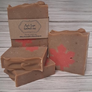 May include: Several bars of handmade soap with a maple sugar scent. The soap is light brown with a red maple leaf design. One bar has a brown paper label that reads "Maple Sugar handmade soap" and "Blackwell's Boutique". Each bar weighs 4.06 oz.