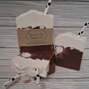 May include: Handmade root beer float soap bars with white, brown, and black accents. The soap bars are designed to look like root beer floats, complete with a white foamy top and a black and white polka dot straw.