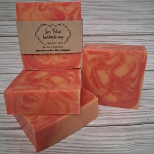 May include: Three rectangular bars of handmade soap with a marbled orange and pink pattern. One bar features a brown paper label with the text Love Potion handmade soap, Net wt. 4.1oz/116g, and Blackwell's Boutique printed in black ink.