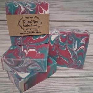 May include: Handmade soap bars with a swirled design in shades of teal, red, and white. The soap is labeled "Torrential Rains" and is from Blackwell's Boutique. Each bar weighs 4.16 oz (118g).