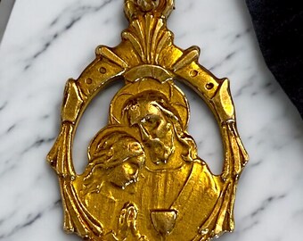 May include: Gold-toned pendant featuring a religious image of Jesus Christ holding a chalice with a child kneeling before him. The pendant is in an ornate oval frame with a loop at the top for hanging.