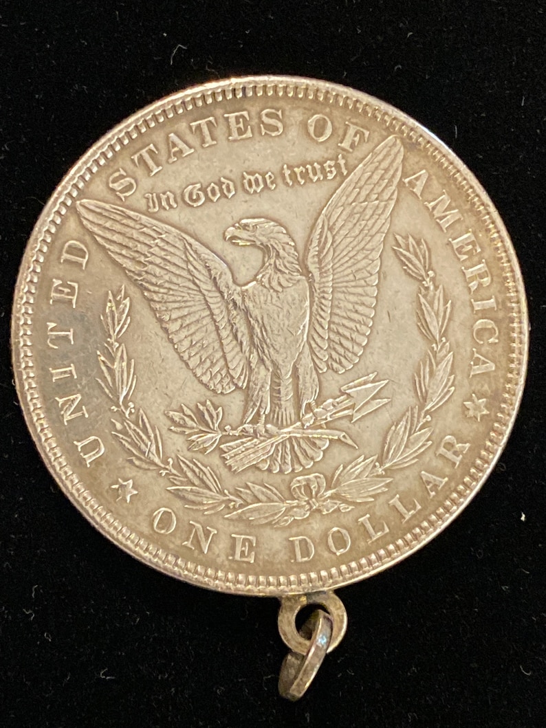 May include: Silver dollar coin with a bald eagle and the words "United States of America" and "In God We Trust" on the front. The coin has a loop on the bottom for hanging.