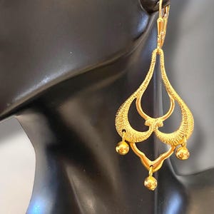 May include: Gold dangle earrings with a teardrop shape and multiple small round beads hanging from the bottom.