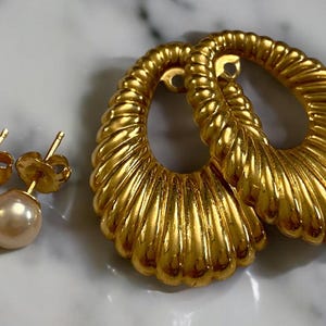 Pu&ograve; includere: Un set di orecchini in oro con un paio di grandi orecchini ovali con un design testurizzato a forma di conchiglia e un paio di piccoli orecchini a perno di perla.