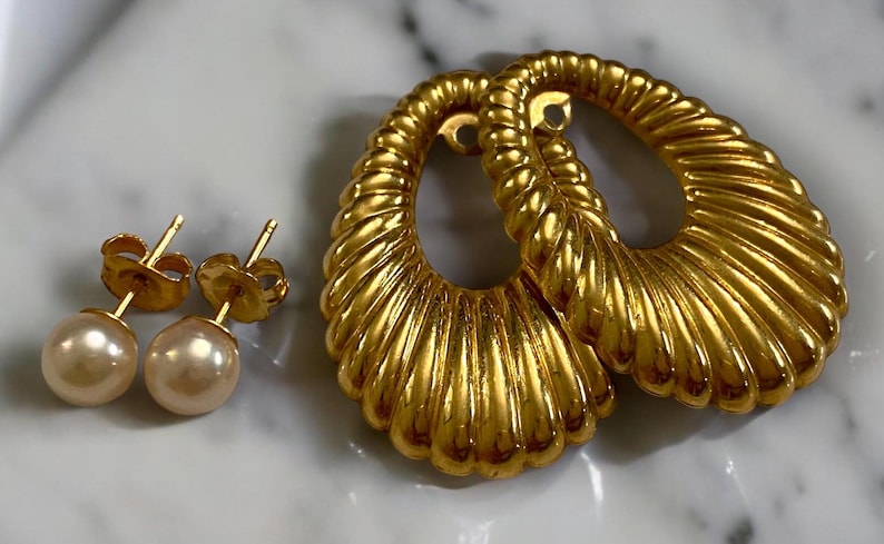 Pu&ograve; includere: Un set di orecchini in oro con un paio di grandi orecchini ovali con un design testurizzato a forma di conchiglia e un paio di piccoli orecchini a perno di perla.