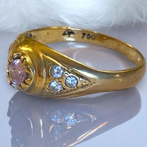 Pu&ograve; includere: Un anello d'oro con una pietra preziosa rosa e tre pietre preziose pi&ugrave; piccole trasparenti. L'anello &egrave; contrassegnato con "750" all'interno.