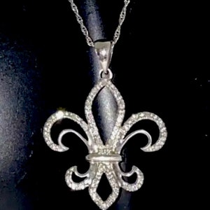 Può includere: Una collana con ciondolo in argento a forma di giglio. Il ciondolo è decorato con piccole pietre trasparenti che creano un effetto scintillante.