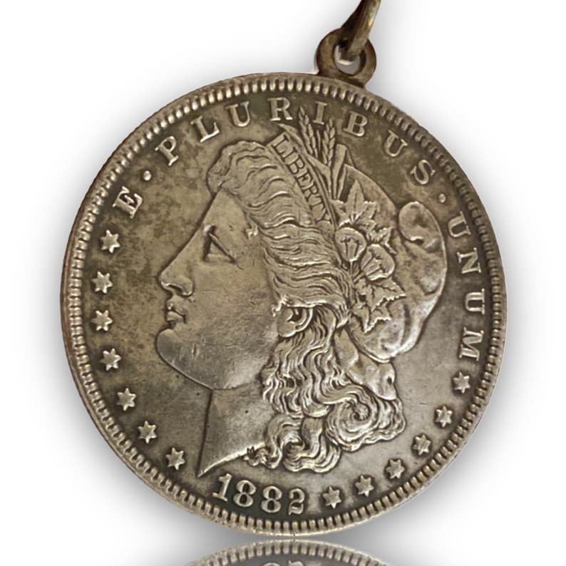 May include: A silver dollar coin with a portrait of Liberty on one side and the words "E Pluribus Unum" on the other. The coin is dated 1882.