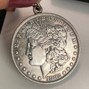 May include: Silver dollar coin with the profile of a woman's face and the words "E Pluribus Unum" and "Liberty" on the front. The coin is dated 1882.