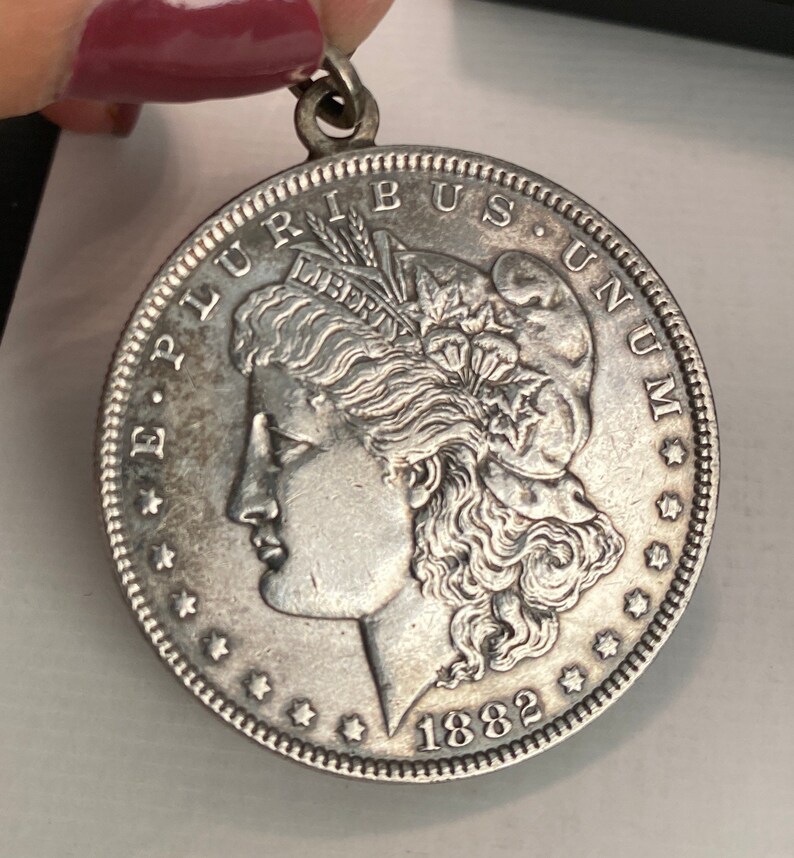 May include: Silver dollar coin with the profile of a woman's face and the words "E Pluribus Unum" and "Liberty" on the front. The coin is dated 1882.
