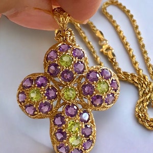 Può includere: Una collana con catena d'oro con un ciondolo a forma di croce. La croce è adornata con pietre preziose viola e verdi.