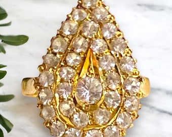 May include: A gold ring with a teardrop-shaped setting encrusted with small, clear gemstones.