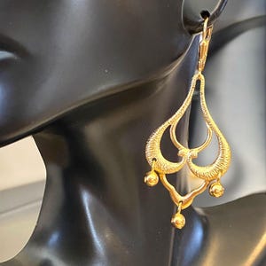 May include: Gold dangle earrings with a teardrop shape and multiple small round beads hanging from the bottom.