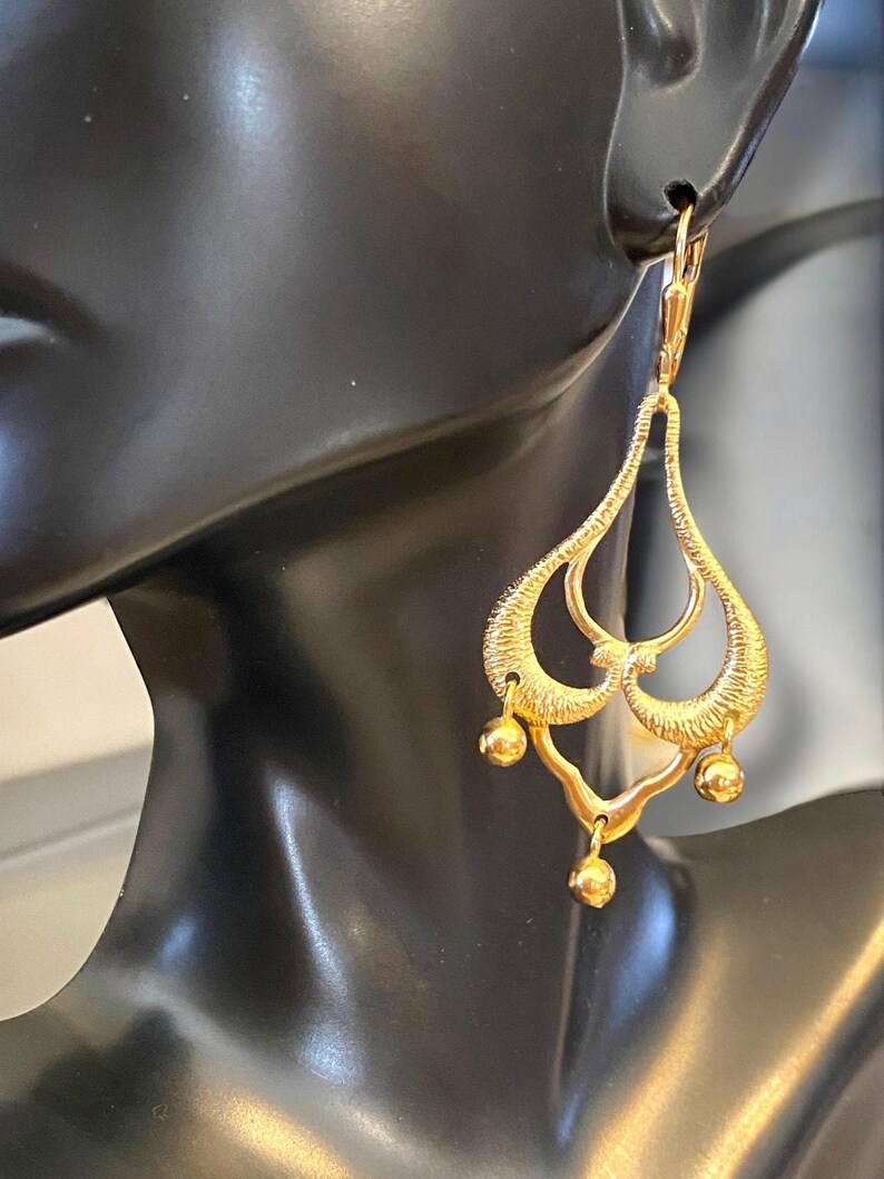 May include: Gold dangle earrings with a teardrop shape and multiple small round beads hanging from the bottom.