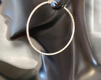 May include: Silver hoop earrings with a textured, braided design. The hoops are large and circular.