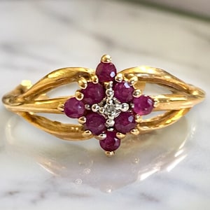 May include: A gold ring with a cluster of red rubies and a single diamond in the center. The ring has a delicate, twisted band.