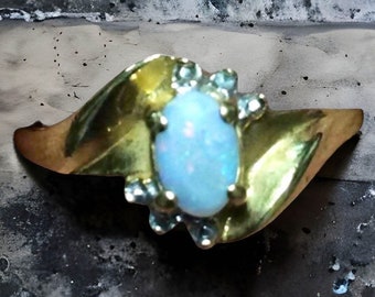 Op de afbeelding: Een gouden ring met een grote ovale opaal-edelsteen, omringd door kleinere diamanten. De ring heeft een gedraaide band.