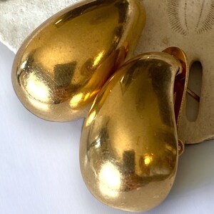 May include: A pair of gold-tone teardrop-shaped earrings. The earrings are smooth and shiny.