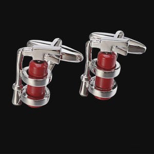 May include: A pair of silver-toned cufflinks with a red fire extinguisher design. The cufflinks have a detailed, miniature replica of a fire extinguisher, with silver accents and a classic toggle closure. The background is solid black.