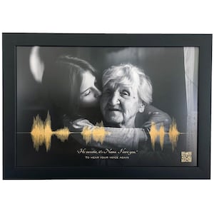 Peut inclure: Un cadre noir contenant une photographie en noir et blanc d'une personne jeune embrassant une personne âgée. Un graphique d'onde sonore dorée est superposé à l'image, avec le texte "Hi sweetie, it's Nana. I love you." et un code QR.
