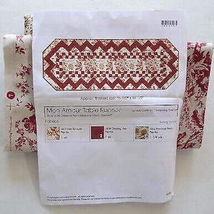 Könnte beinhalten: Ein Tischläufermuster mit einem rot-cremefarbenen Blumenmuster, zusammen mit passenden Stoffen. Das Muster trägt die Bezeichnung "Mon Amour Table Runner" und hat eine ungefähre Größe von 42 x 113 cm.
