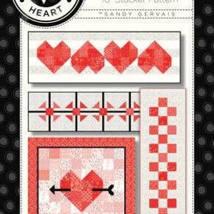 May include: A quilt pattern named "On Top of It" featuring red and white designs, including hearts and an arrow through a heart. The pattern is for a 10-inch stacker, with measurements of approximately 25 cm.