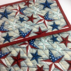 May include: Two red and white quilted placemats with a blue and white star pattern. The placemats have a red border.