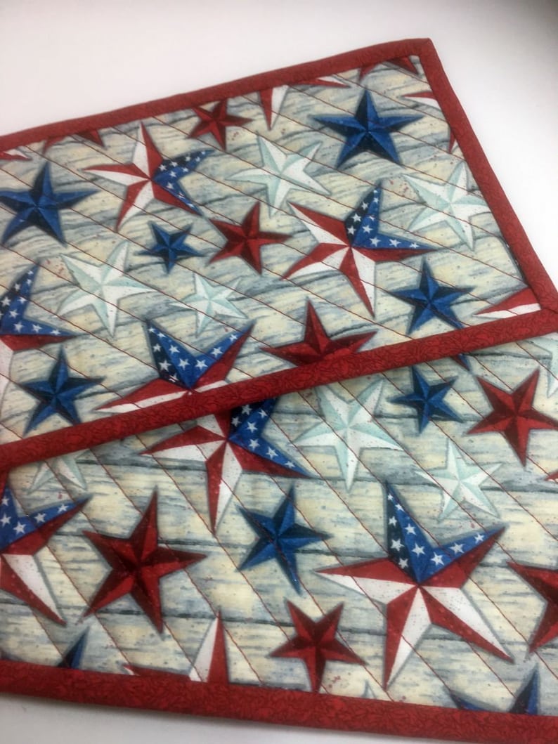 May include: Two red and white quilted placemats with a blue and white star pattern. The placemats have a red border.