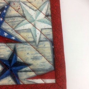 May include: Close-up of a red, white, and blue fabric with a star pattern. The fabric has a red border with a floral pattern.