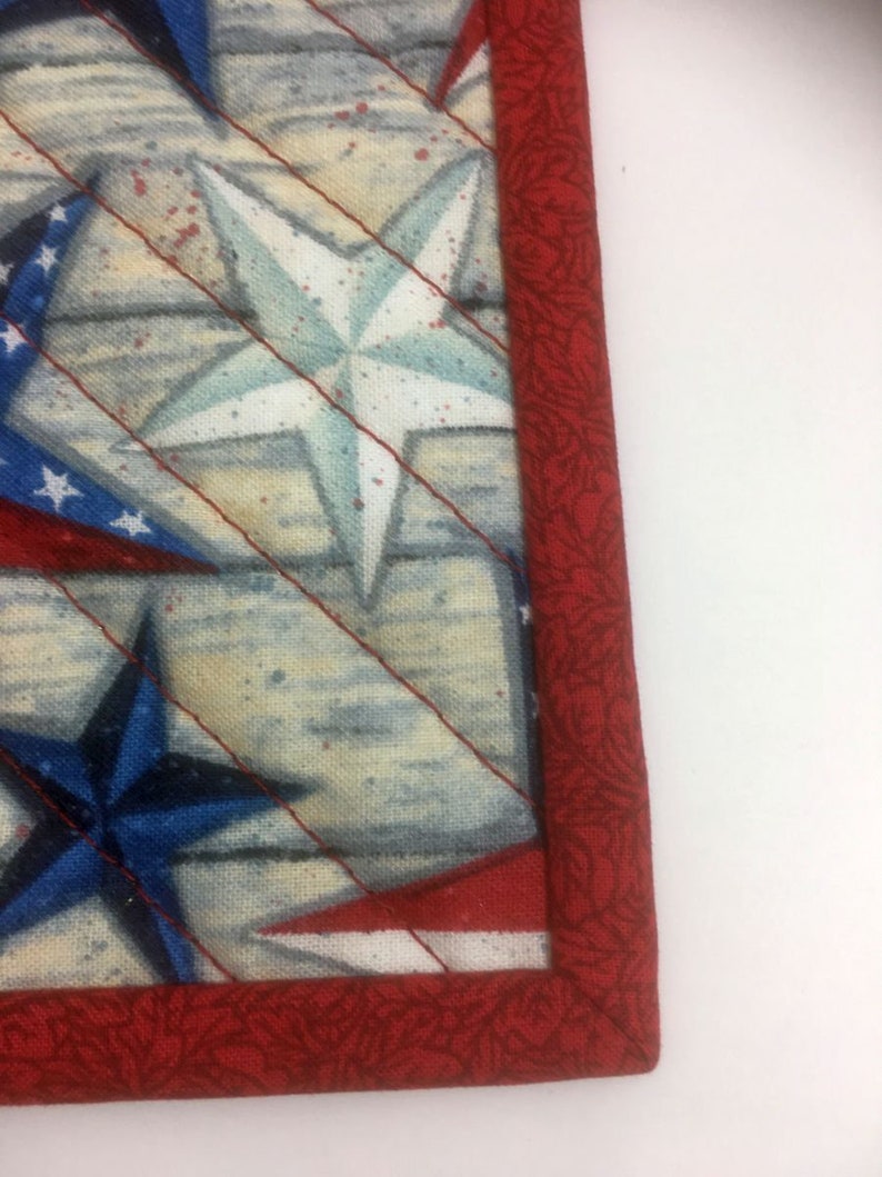 May include: Close-up of a red, white, and blue fabric with a star pattern. The fabric has a red border with a floral pattern.