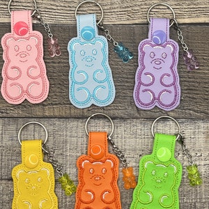 May include: Six colorful gummy bear keychain charms. Each charm is made of felt and features a gummy bear design with a small gummy bear charm attached to a silver chain. The charms are pink, blue, purple, yellow, orange, and green.