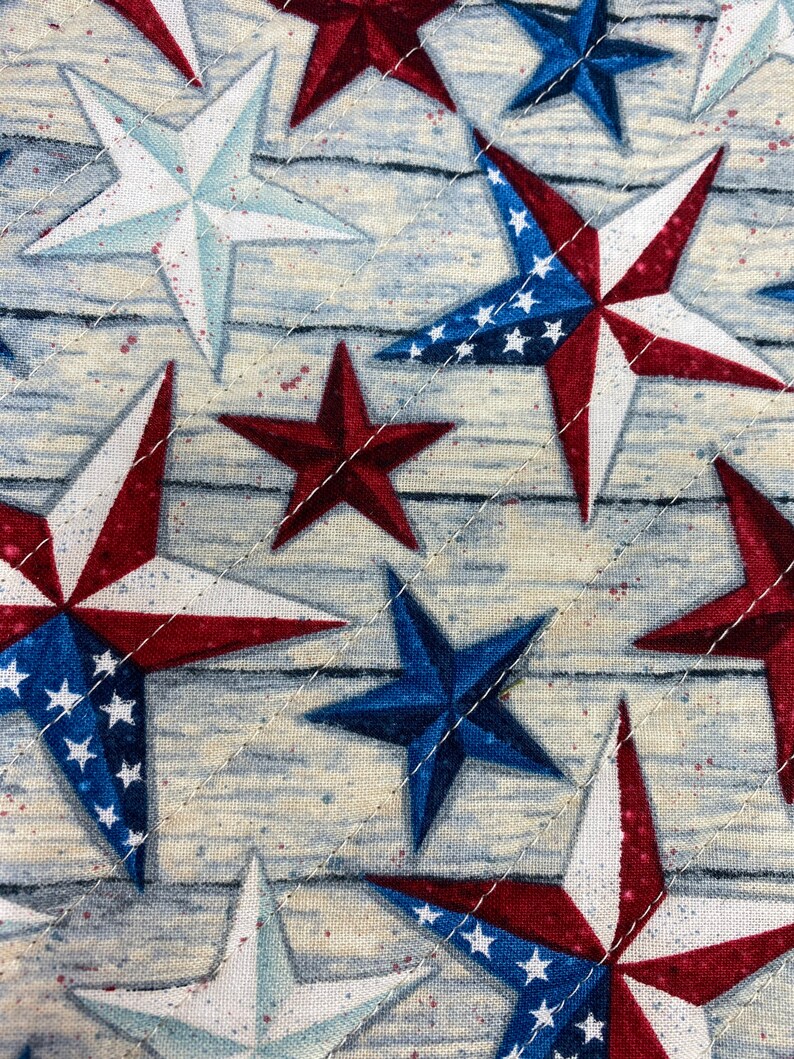 May include: A close-up of a fabric with a repeating pattern of red, white, and blue stars. The stars are arranged in a diagonal pattern on a light blue background.