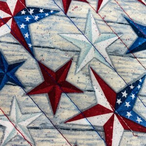 May include: A close-up of a fabric with a repeating pattern of red, white, and blue stars. The stars are arranged in a diagonal pattern on a light blue background.