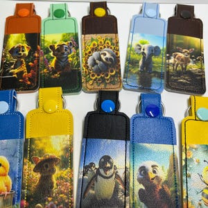 May include: A collection of colorful keychains featuring various animal illustrations. Each keychain has a different color top and a button closure. The animal images include a puppy, tiger, sloth, elephant, deer, chick, bear, penguin, and bee.