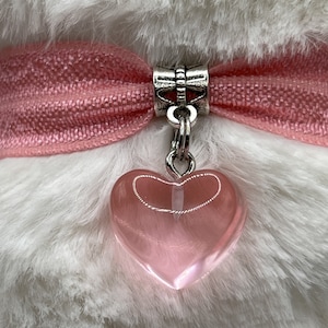 May include: A pink heart-shaped charm with a silver chain and a silver clasp attached to a pink ribbon.