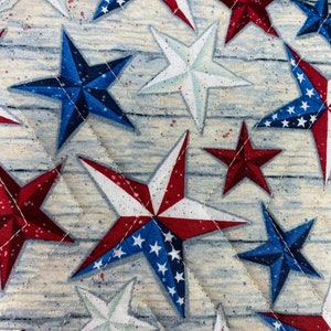 May include: A quilted fabric with a repeating pattern of red, white, and blue stars. The stars are in various sizes and orientations, and some have a white background with blue stars.
