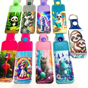 May include: A collection of colorful keychains featuring various animal and fantasy character designs. Each keychain has a leatherette top with a metal ring and a printed design on the front, including a panda, koala, puppy, dog, sloth, flamingo, unicorn, cat, and frog.