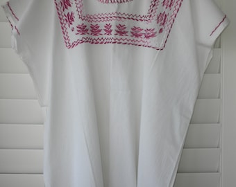 May include: White cotton blouse with a pink embroidered neckline. The embroidery features a geometric pattern with floral motifs.