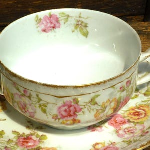 May include: A white porcelain teacup and saucer with a gold rim and floral pattern. The cup has two handles and the saucer has a scalloped edge.
