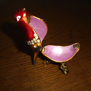 May include: A red, white, and blue bird-shaped trinket box with a pink interior. The box is open and the bird's head is tilted back.