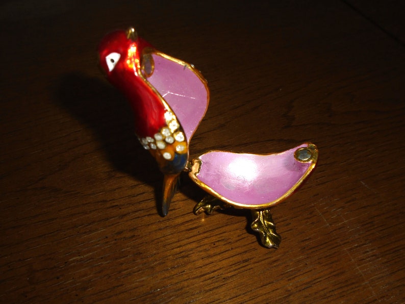 May include: A red, white, and blue bird-shaped trinket box with a pink interior. The box is open and the bird's head is tilted back.