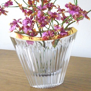 May include: A clear glass vase with a gold rim, filled with vibrant purple and yellow orchids. The vase has a fluted design and sits on a wooden surface, creating a striking floral arrangement.