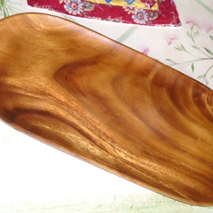 May include: A wooden serving tray with a natural wood grain finish. The tray is oval-shaped and measures approximately 18 inches long. The wood has a warm, reddish-brown hue, with darker streaks and patterns throughout the surface.