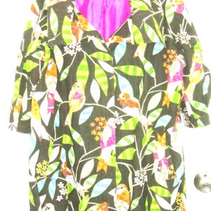 May include: A long-sleeved coat featuring a dark brown base with a vibrant pattern of colourful birds, green leaves, and small white flowers. The garment has a bright pink interior lining and a visible label at the neckline with the text "M".