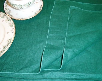 Puede incluir: Una servilleta de lino verde doblada con una textura sutil. La servilleta está doblada en tres y tiene un borde ligeramente deshilachado.