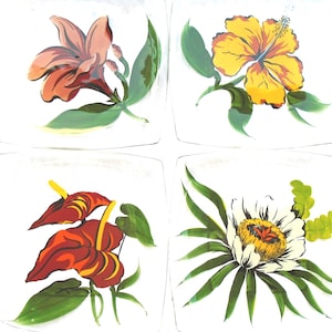Puede incluir: Un juego de cuatro platos cuadrados de cristal, cada uno con una ilustración botánica distinta. Los diseños incluyen un lirio rosa, un hibisco amarillo, flores de anturio rojas y una pasionaria blanca, acompañadas de hojas verdes.