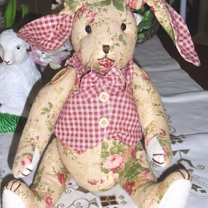 May include: A handmade patchwork bunny rabbit toy with a floral print and a red and white gingham vest. The bunny has a white face and long ears.