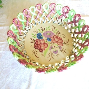 May include: A white ceramic bowl with a woven design in pink, green, and white. The bowl has a floral design in the center with pink, green, blue, and white flowers.